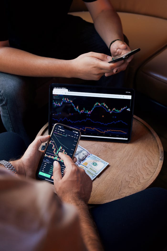 Two people using smartphone and tablet for trading stocks indoors.